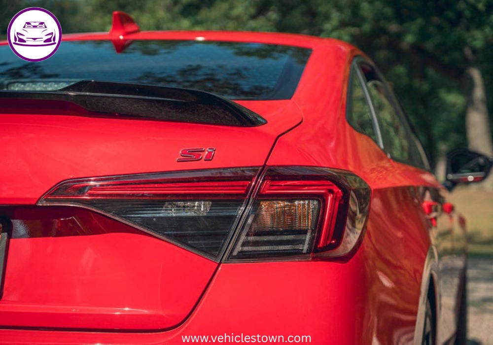 Honda Civic Si sporty red sedan parked, showcasing aggressive front grille and alloy wheels.