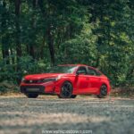 Honda Civic Si sporty red sedan parked, showcasing aggressive front grille and alloy wheels.
